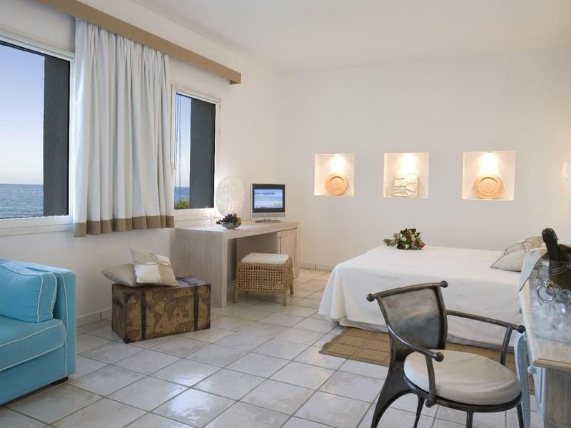 Helles Hotelzimmer mit Balkon, Doppelbett, blauem Sofa und Schreibtisch mit Stuhl.