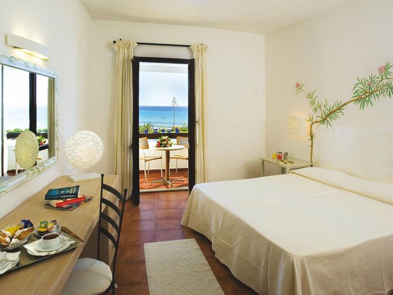 Helles Hotelzimmer mit Doppelbett, Schreibtisch, Stühlen, Balkon und Meerblick bei Tageslicht.