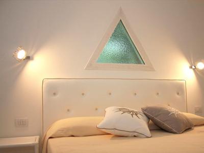 Schlafzimmer mit beige Bett, gepolstertem Kopfteil, zwei Kissen und dreieckigem Fenster oberhalb.