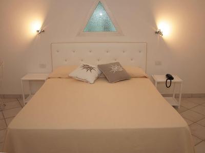 Einfaches Schlafzimmer mit Doppelbett, beigefarbener Decke und drei Kissen unter einem dreieckigen Fenster.