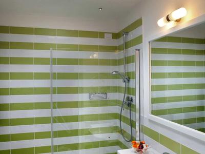 Badezimmer mit grünen und weißen Kacheln, Dusche mit Glaswand, Waschbecken und großem Spiegel.