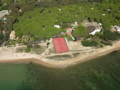 Luftaufnahme eines waldbedeckten Küstenabschnitts mit rotem Tennisplatz und grünem Meer.