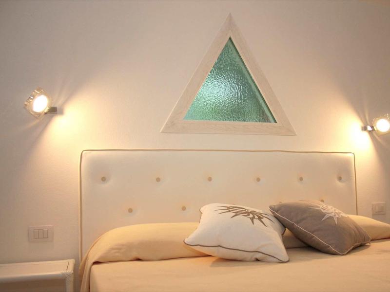 Schlafzimmer mit beige Bett, gepolstertem Kopfteil, zwei Kissen und dreieckigem Fenster oberhalb.