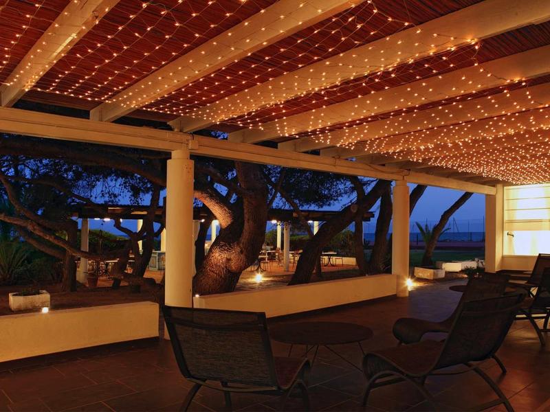 Überdachte Terrasse mit warmen Lichterketten, zwei Stühlen und großem Baum im Hintergrund bei Dämmerung.