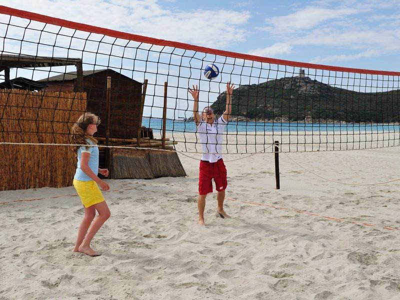 Zwei Kinder spielen Beachvolleyball auf sandigem Strand unter blauem Himmel mit leichter Bewölkung.