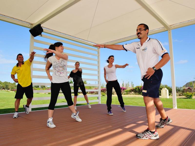 Fünf Menschen trainieren unter einem Pavillon draußen bei klarem Himmel, tragen sportliche Kleidung.