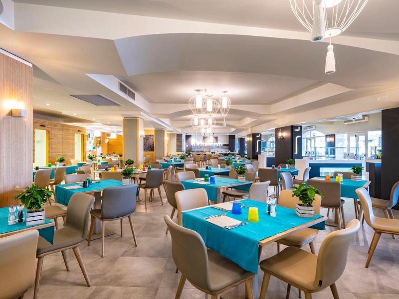 Großer, moderner Speisesaal mit blauen Tischdecken, grauen Stühlen und hellen Deckenleuchten.