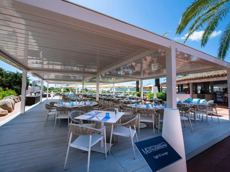 Moderner Außenbereich mit gedeckten Sitzplätzen, weißen Stühlen und blauen Tischdekorationen unter Überdachung.