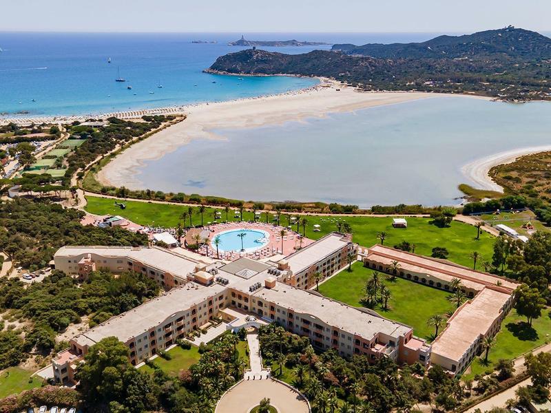Großer Pool mit umliegenden Gebäuden und Lagune am Meer, Umgeben von grüner Vegetation.