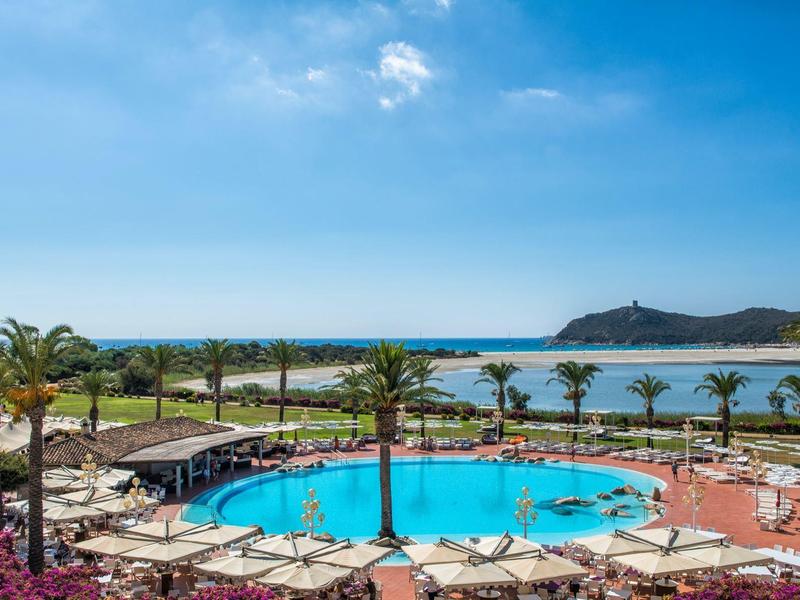 Runder Pool mit Liegen umgeben, Palmen und Meer im Hintergrund unter blauem Himmel.