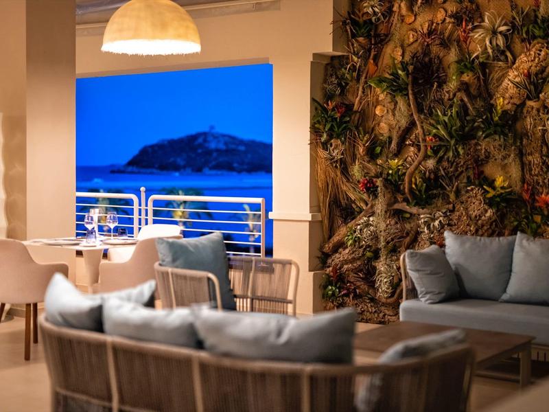 Moderner Außenbereich mit grauen Sofas, Holzmöbeln, Pflanzenwand und Blick auf beleuchteten Hügel.