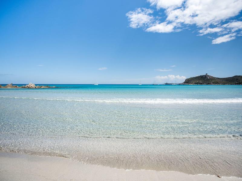 Klares, flaches Meer mit weißem Sandstrand und bewölktem Himmel, weiter Horizont mit Hügeln.