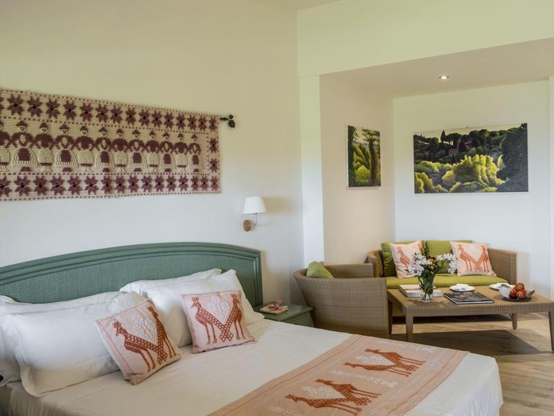 Lichte slaapkamer met groen bed, decoratieve kussens en een gezellige zithoek met bank.