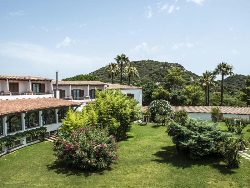 Een hotel met groene buitenruimte en heuvels op de achtergrond onder een blauwe lucht.