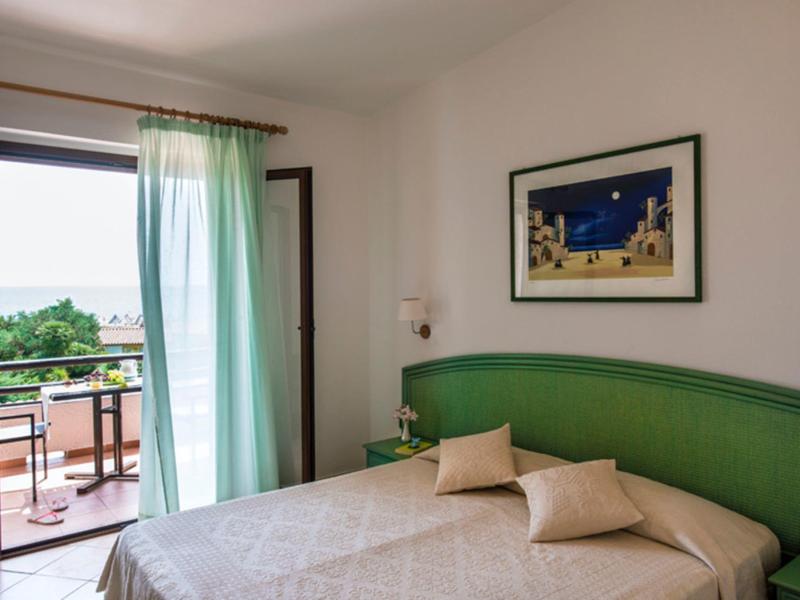 Lichte hotelkamer met tweepersoonsbed, groene hoofdbord en balkon met uitzicht op groen.