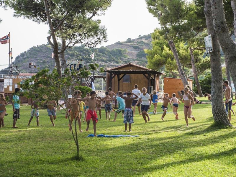 Kinderen spelen op een grasveld bij een camping met bomen en hutten.