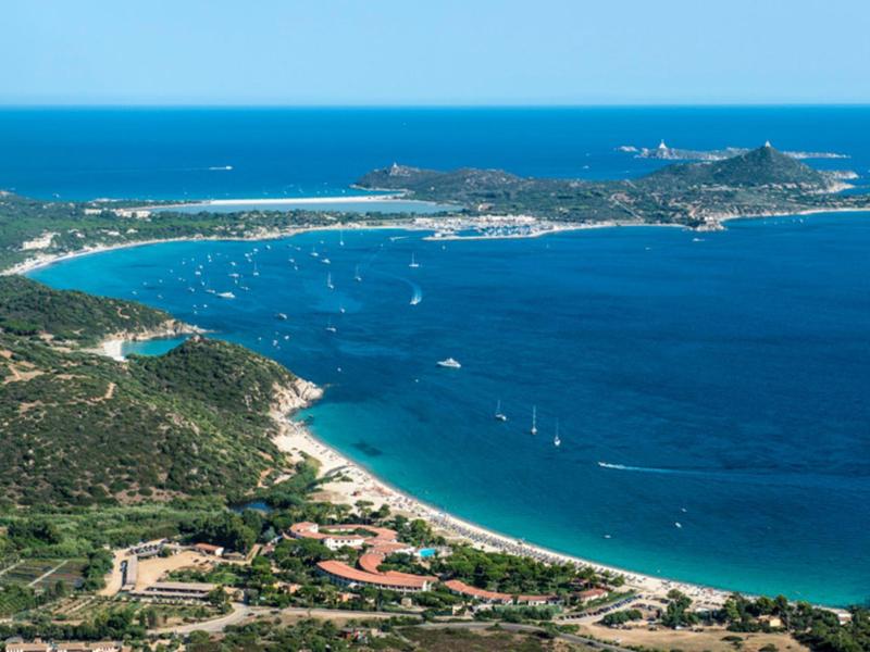Luchtfoto van een kustbaai met strand, boten en eiland op de achtergrond.