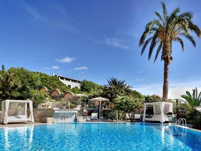 Area piscina con lettini, letti a baldacchino bianchi e una palma alta sotto un cielo sereno.