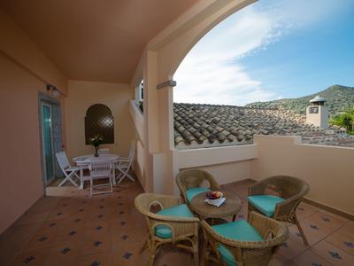 Cozy balcony with seating area overlooking hills and village under a blue sky.