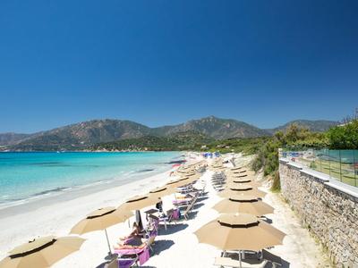 Beach with sun loungers and umbrellas by turquoise sea and mountains in the background.