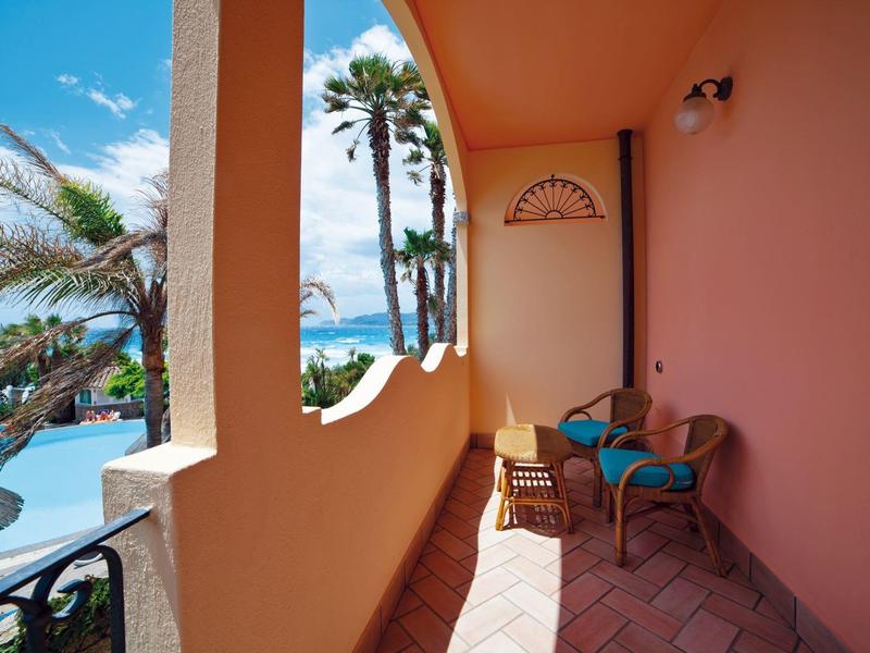 Balcony with chairs, view of palm trees and ocean under blue sky