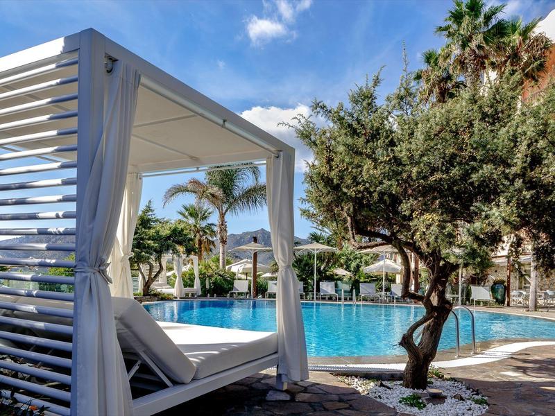 Luxurious pool area with lounge bed and tropical plants under a blue sky.