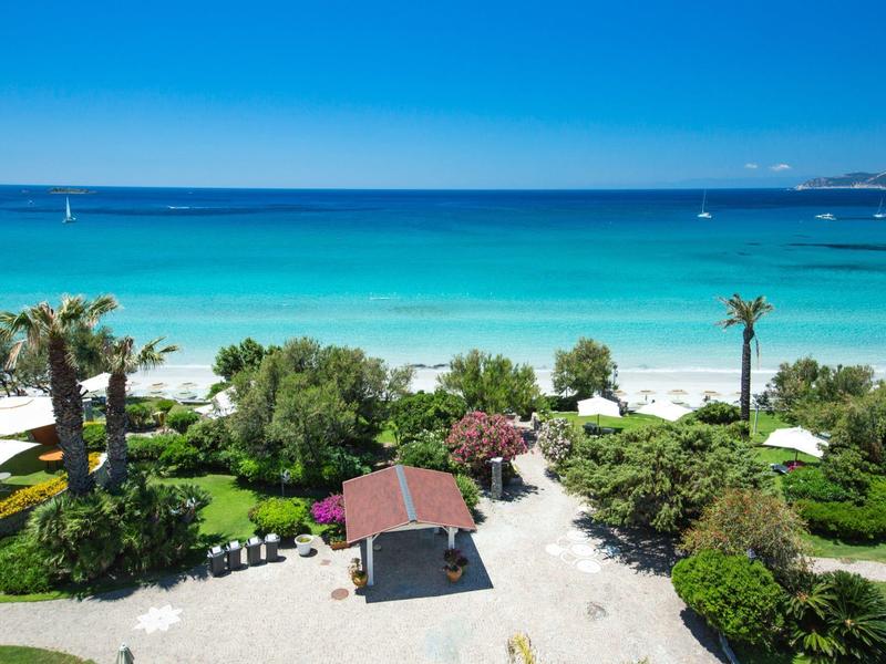 View of a tropical beach with turquoise water, palm trees, and a small pavilion.