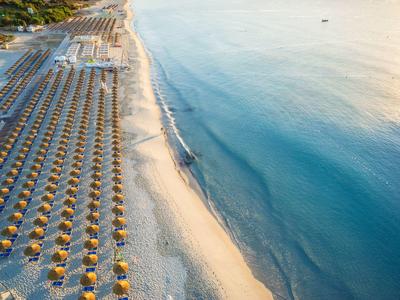 Lange zandstrand met rijen parasols en ligstoelen naast kalme zee.