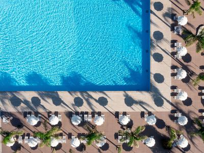Vogelperspektive eines Pools mit Liegestühlen und Sonnenschirmen am Rand.