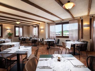 Lichte eetzaal met houten balken, tafels met witte tafelkleden en grote ramen met uitzicht.