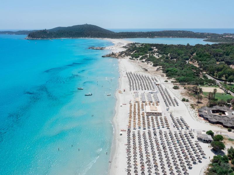 Lange wit zandstrand met rijen parasols en helder turquoise water.