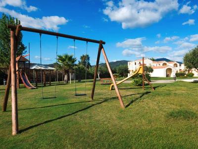 Plac zabaw z huśtawkami na zielonej trawie przed dużym białym budynkiem pod niebieskim niebem.