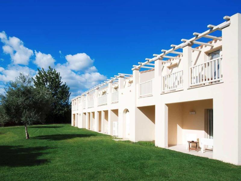 Nowoczesny kompleks hotelowy z białymi balkonami i zielonym trawnikiem pod niebieskim niebem.