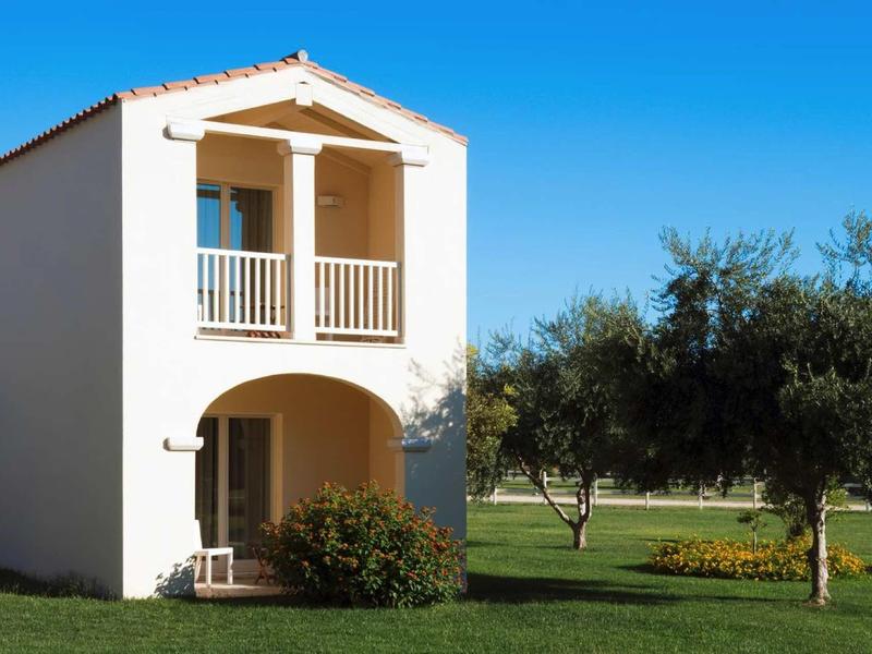 Dwupiętrowy domek letniskowy z balkonem i ogrodem pod jasnym, niebieskim niebem.