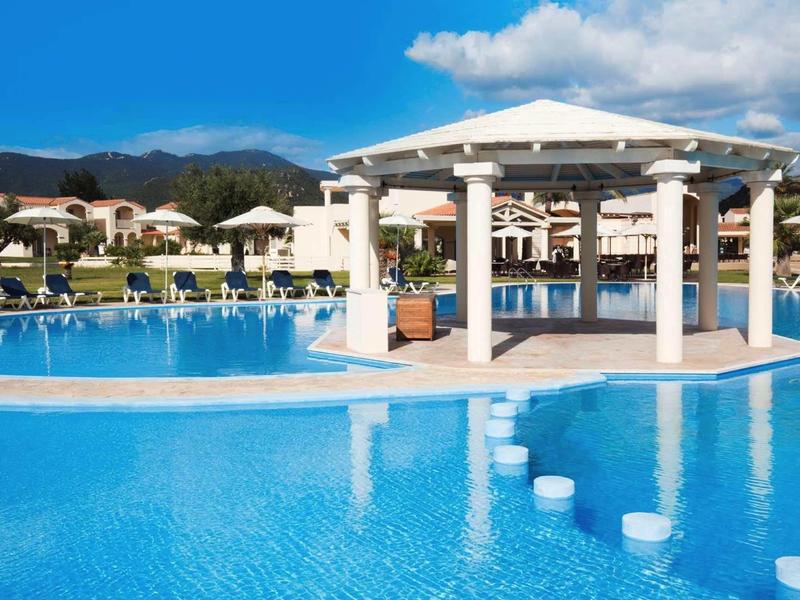 Duży basen z barem swim-up i leżakami na tle gór pod czystym niebem.