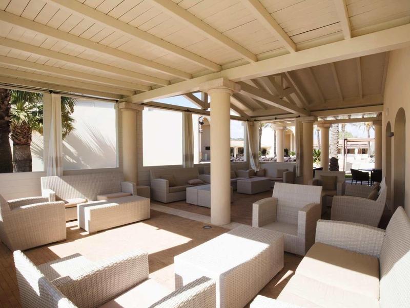 Zadaszona przestrzeń wypoczynkowa z białymi meblami i kolumnami w jasnym, słonecznym pomieszczeniu.