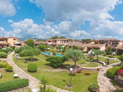 Große Gartenanlage mit vielen Wegen, grünen Büschen und mediterranen Häusern unter blauem Himmel.