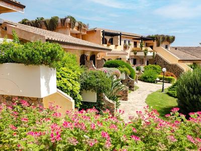 Mediterrane Wohnanlage mit hellen Häusern, gepflegten Gärten und bunten Blumen unter blauem Himmel.