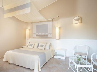 Helles Schlafzimmer mit Doppelbett, weißen Möbeln, zwei Stühlen und sanfter Beleuchtung.