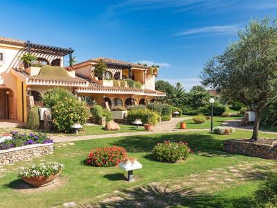 Mediterrane Hotelanlage mit gepflegten Gärten und blühenden Pflanzen unter blauem Himmel.