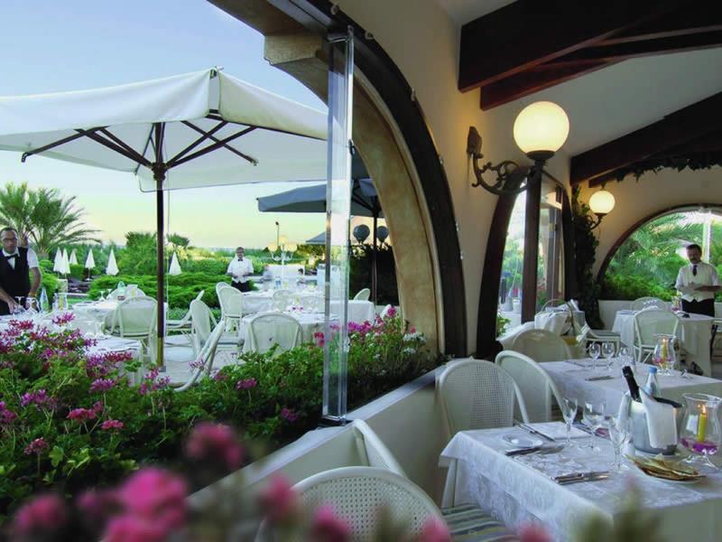 Elegantes Außenrestaurant mit weißen Tischen, Stühlen, blühenden Pflanzen und großen Sonnenschirmen.