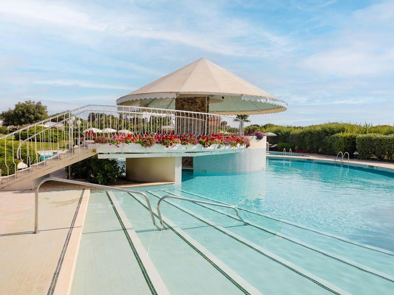 Moderner Außenpool mit runder Bar, breiten Treppen, Geländer und blumenverzierten Balkonen.