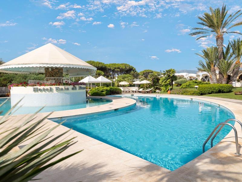 Großer Pool mit klarem Wasser, umliegenden Pflanzen und Sonnenschirm unter blauem Himmel.