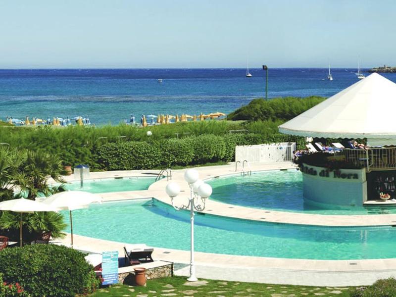 Pool mit Rundbar, Liegestühlen und grüner Bepflanzung am Meer bei klarem Himmel.