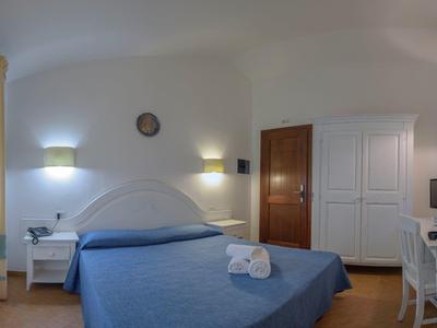 Hell eingerichtetes Hotelzimmer mit Doppelbett, Schreibtisch, Stuhl und Fenster mit Gardinen
