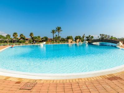 Großer Pool mit klarem Wasser und Palmen im Hintergrund bei sonnigem Wetter.