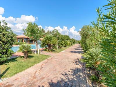 Gepflasterter Weg neben Grünflächen und Pool unter blauem Himmel mit Wolken.