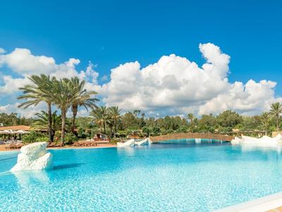Großer Pool mit klarem Wasser, Palmen und blauem Himmel mit Wolken.