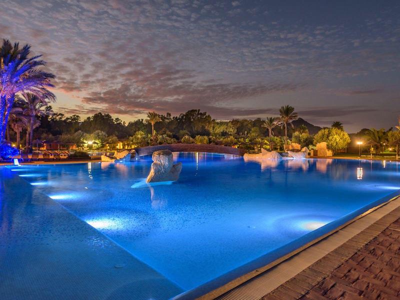 Beleuchteter Hotelpool bei Nacht mit Palmen und Sternenhimmel