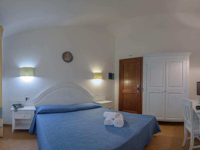 Hell eingerichtetes Hotelzimmer mit Doppelbett, Schreibtisch, Stuhl und Fenster mit Gardinen